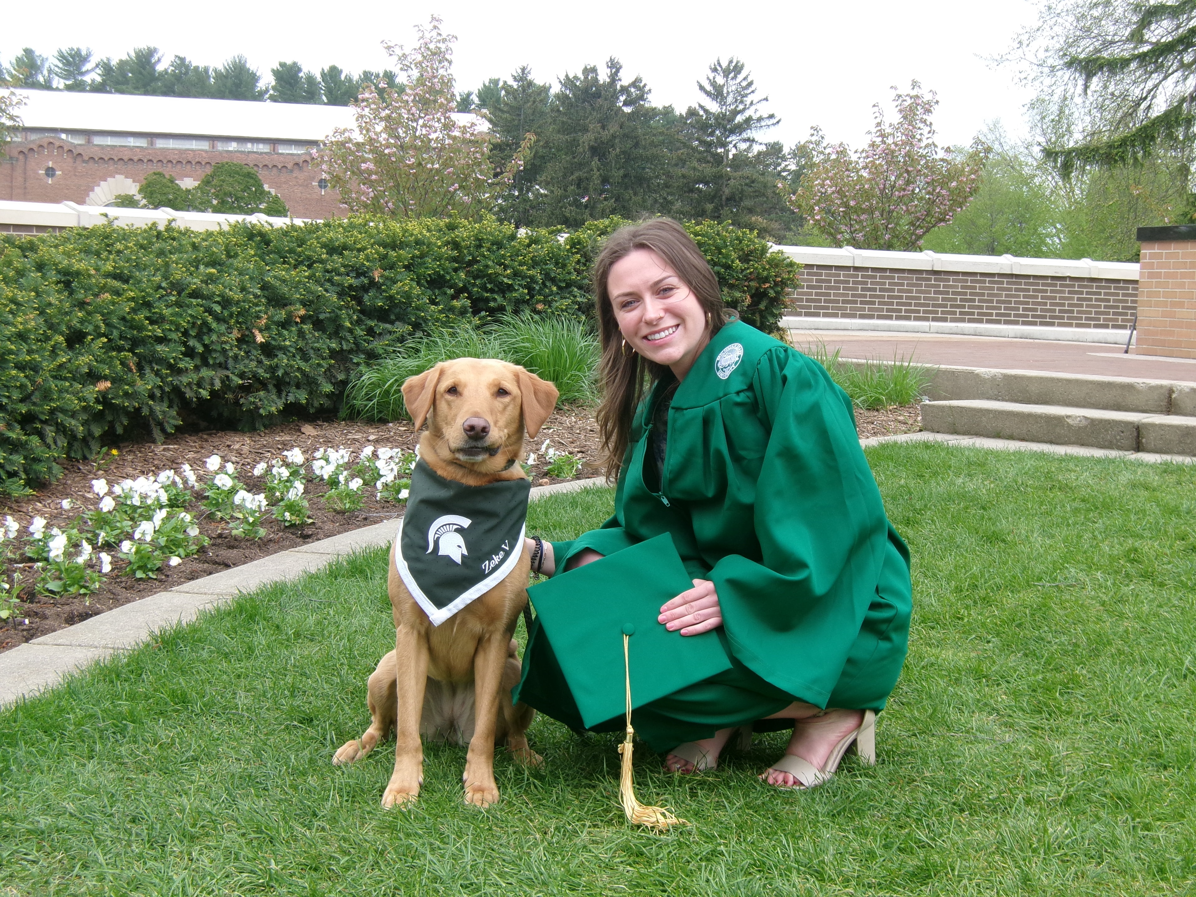 MSU graduate posing with Zeke and a graduation cap on campus